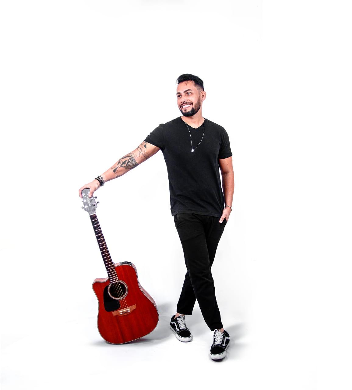 Ricky Moreira em pé ao lado do violão